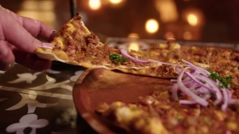 Hand taking a slice of lahmacun from a wooden plate in a Turkish restaurant Stock Footage 345146096