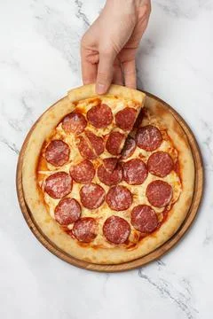 Hand taking a slice of pepperoni pizza on a gray background Stock Photos