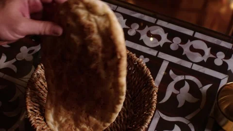 Hand taking a traditional Turkish flatbread from a basket on an ornamental table Stock Footage 345146082