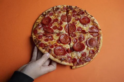 Hand taking a triangular slice of a pepperoni pizza Stock Photos