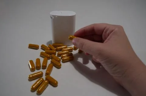 Hand Taking Yellow Capsule Next to White Container Stock Photos