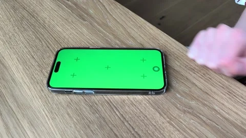 Hand taps a smartphone with green screen on a wooden table. Finger interact.. Stock Footage 334723245