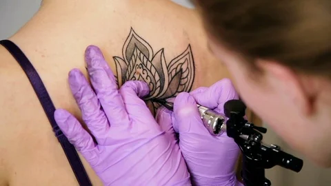 Hand with a tattoo machine makes a lotus flower on a woman's back Stock Footage 73419113