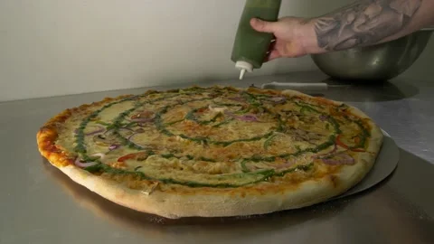 The hand of a tattooed chef adding green sauce to a very large pizza 60fps 4K Stock Footage 192456562