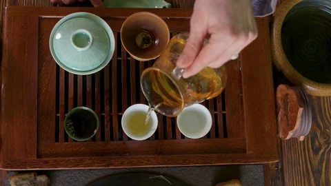 Hand of tea master pouring green oolong brewing tea from glass pot to tea bowl. Stock Footage 241012598