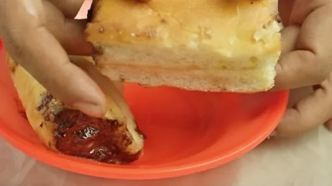 Hand tearing chocolate roll bread apart on an orange plate Video stock 323572581