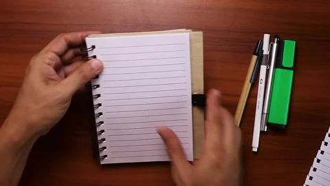 Hand tearing a page with notes out of a spiral notebook on a wooden table. Stock Footage 337911493
