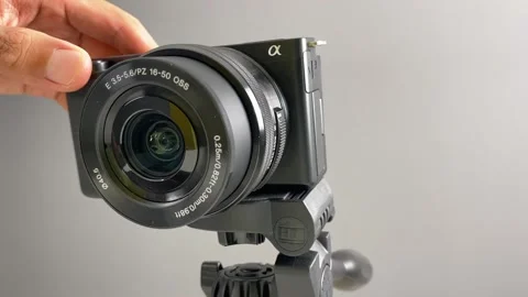Hand testing zooming lens of SONY camera ZV-E10 on tripod indoor Stock Footage 250792602