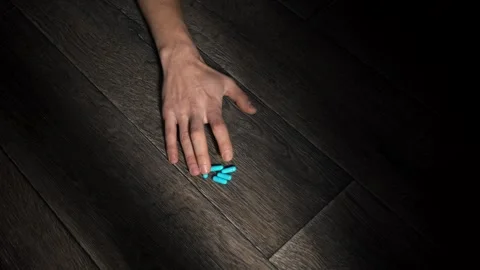 Hand of a thin man reaches out to the blue pills scattered on the floor. Stock Footage 260568568