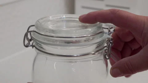 Hand Thoughtfully Opens Clear Glass Jar, Securing Freshness in Home Storage Stock Footage 318782214