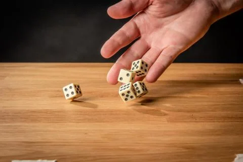 Hand throwing dice in front of a dark background. Stock Photos