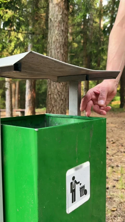 Hand throwing plastic waste into green forest trash bin promoting eco conce.. Stock Footage 343260958