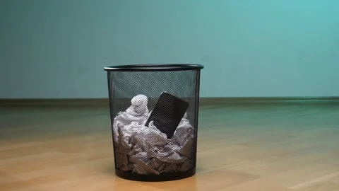 Hand is throwing a smartphone into a trash bin filled with crumpled paper Stock Footage 342760583