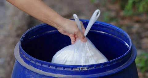 Hand throwing a white plastic garbage bag into a blue bin. waste management Stock Footage 334797476
