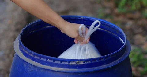 Hand throwing a white plastic garbage bag into a blue bin. Concept of waste Stock Footage 334948553