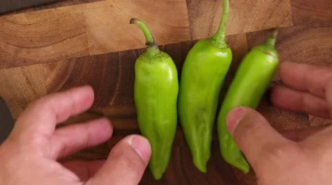 Hand throws and collects big fat green chillies on a wooden cutting board Stock Footage 62823925
