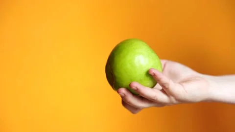 Hand throws an apple on an orange background. green apple in woman's hand Stock Footage 131711733