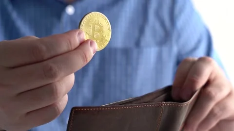 Hand Throws Bitcoin into Wallet. Background Man in Blue Shirt at Home or Office Stock Footage 166996472