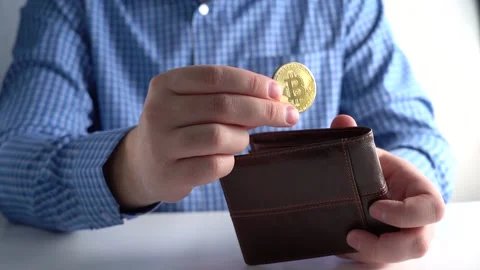 Hand Throws Bitcoin into Wallet. Background Man in Blue Shirt at Home or Office Stock Footage 167885124