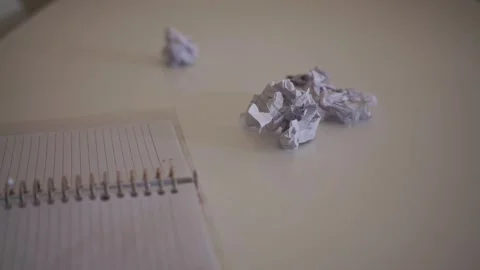 A hand throws a crumpled paper ball onto a desk beside a notebook, symbolizing Stock Footage 340858291