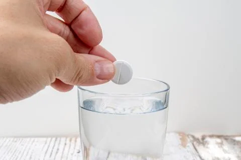 Hand throws an effervescent tablet into a glass of water against a white back Stock Photos