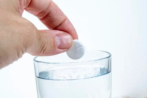 Hand throws an effervescent tablet into a glass of water against a white back Stock-Fotos