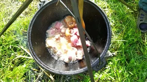 Hand throws meat into a cauldron over an open fire. fry meat outdoors Stock Footage 155684548