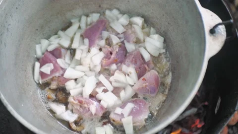 Hand throws meat into a cauldron over an open fire, fry meat outdoors Stock Footage 162582105