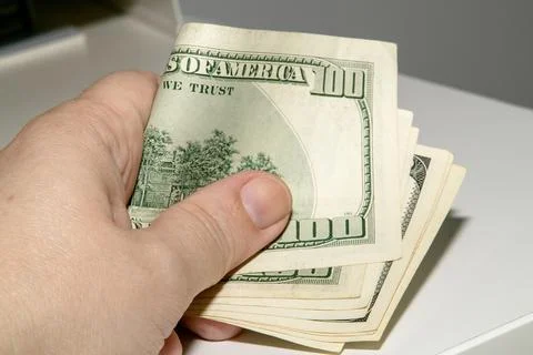 A hand tightly gripping a thick stack of US dollar bills Stock-Fotos
