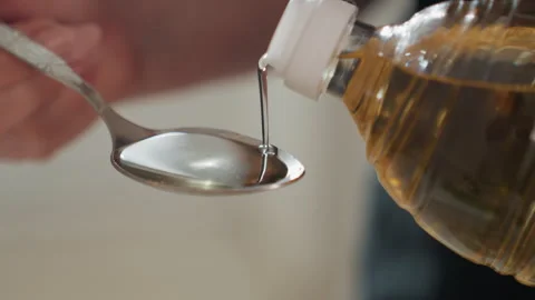 Hand tilting small plastic bottle to pour amber liquid into metal spoon with Stock Footage 343676065