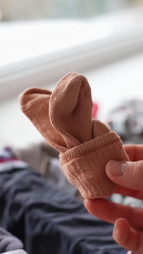 Hand tosses a beige sock toward a laundry basket in soft-focus background Stock Footage 327887047