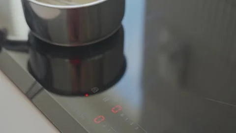 Hand touches control panel on induction cooktop before placing small saucepan Stock Footage 333652878