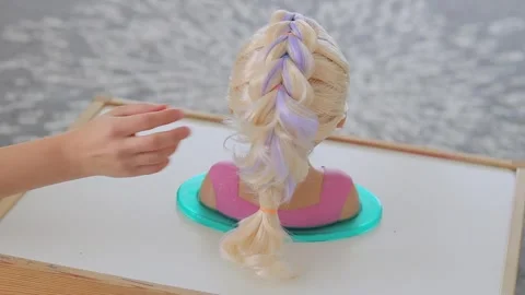 Hand touching dragon braid on child mannequin head with blonde hair Stock Footage 331997400