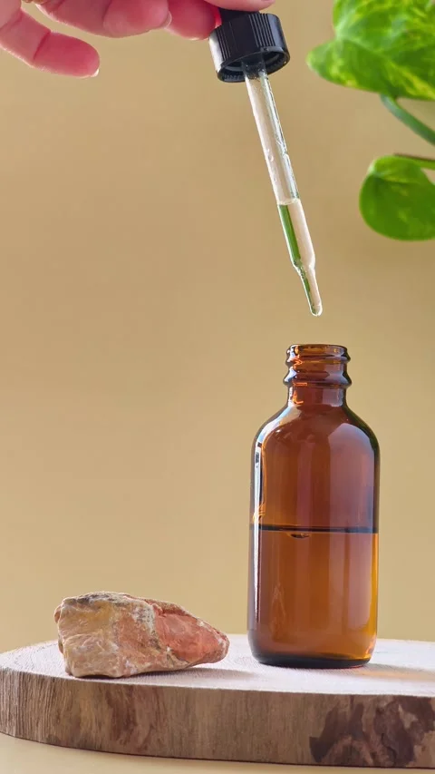 Hand touching dropper on amber glass bottle near natural stone on wood slice. Видео 337101030