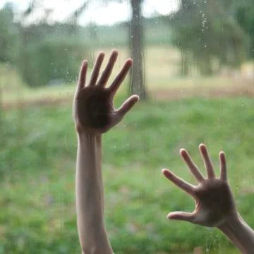 Hand touching a glass window with raindrops over a defocused nature backgroun Stock Photos