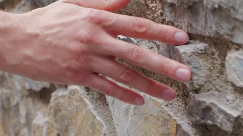 A hand touching a rough stone wall, displaying palm and fingers on the textured Stock Footage 278476883