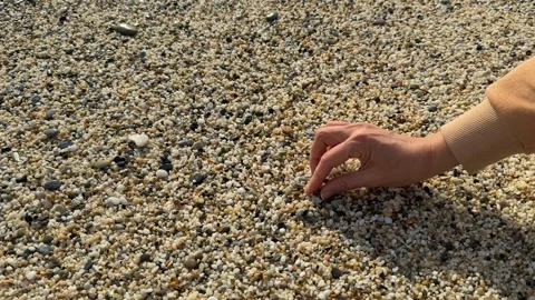 Hand touching small pebbles on a pebble beach, creating a textured background Stock Footage 332354546