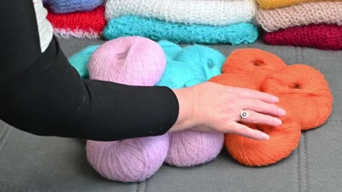 Hand touching soft yarn balls, orange purple wool skeins, craft hobby supplie Stock Footage 334749402