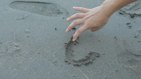 A hand traces lines directly into wet sand at beach Stock Footage 345688907