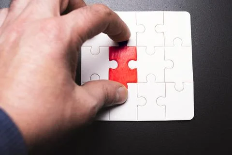 A hand is trying to solve a puzzle with a red piece missing Stock Photos
