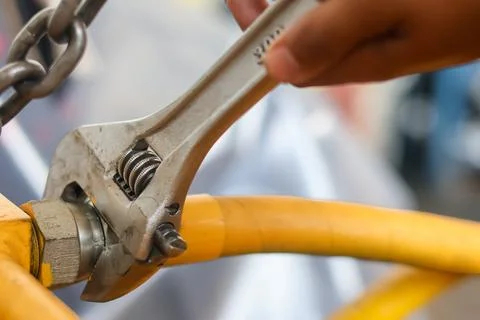Hand turning an adjustable spanner on a yellow fluid line. 스톡 사진