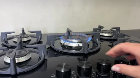 Hand turning the control knob on a modern gas stove with a blue flame burning on Stock Footage 343661900