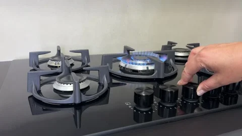 Hand turning the control knob on a modern gas stove with a blue flame burning on Stock Footage 343661906