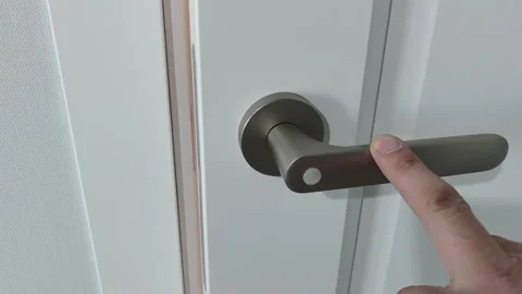 Hand turning a door handle in a home setting during daytime near a plain white d Stock-Footage 329700566