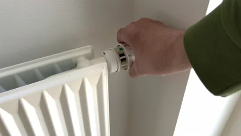 Hand turning down adjusting thermostat on radiator to save energy Stock Footage 188732967