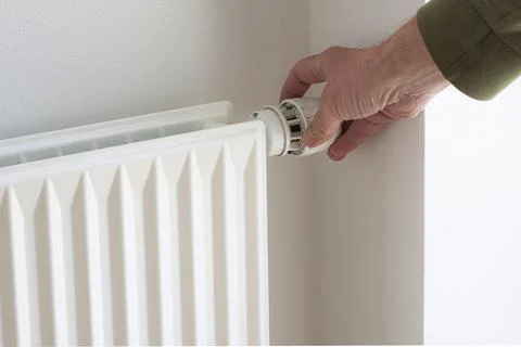 Hand turning down adjusting thermostat on radiator  valve to save energy Stock Photos