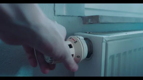 Hand Turning Down Radiator Thermostat to Reduce Heating in Cold Home Video stock 341880386