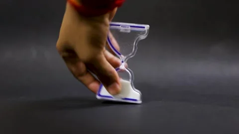 Hand turning Glass timer with sand grains running down representing product.. Stock Footage 318357499