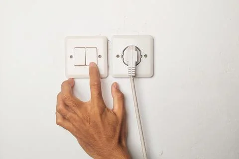 A hand is turning off the light using a wall switch in the house. Stock Photos