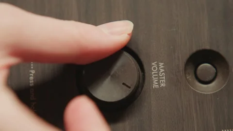 Hand turning master volume knob on wooden audio control panel under warm Stock-Footage 343541081